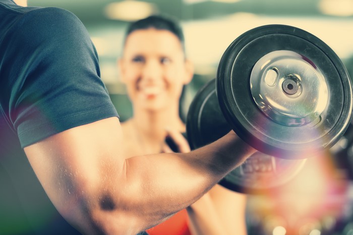 Man lifting dumbbell with woman in background