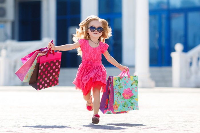 Girl in pink dress running with shopping bags