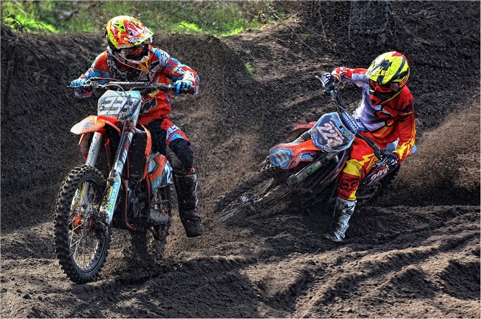 Two motocross riders racing through mud