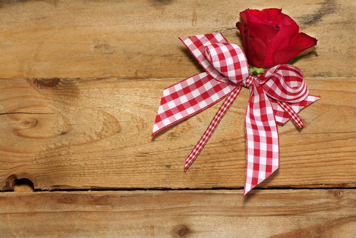 Red rose with a checkered bow on wood