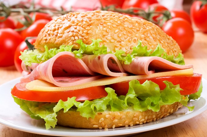 Sandwich with ham, cheese, lettuce, and tomato on a sesame bun