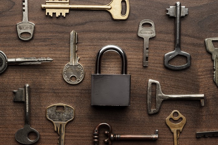 Padlock and various keys on wooden background