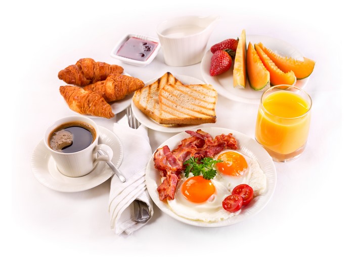 Breakfast with coffee, eggs, bacon, croissants, toast, fruit, and juice