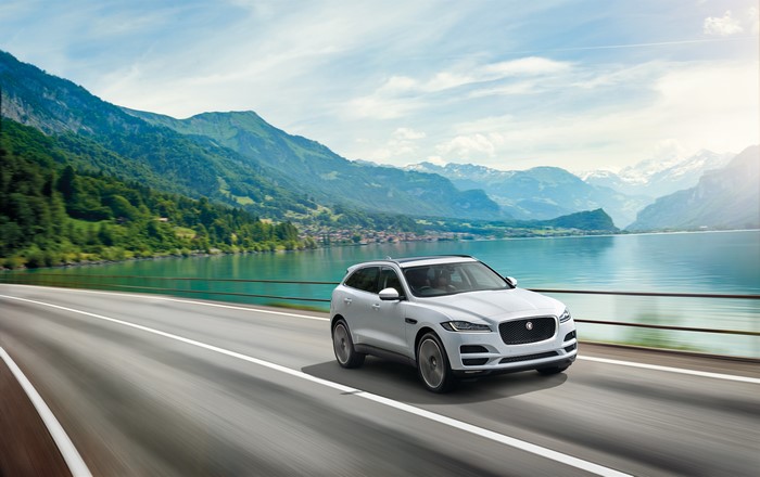 White 2015 Jaguar F-Pace S driving on a road with mountains