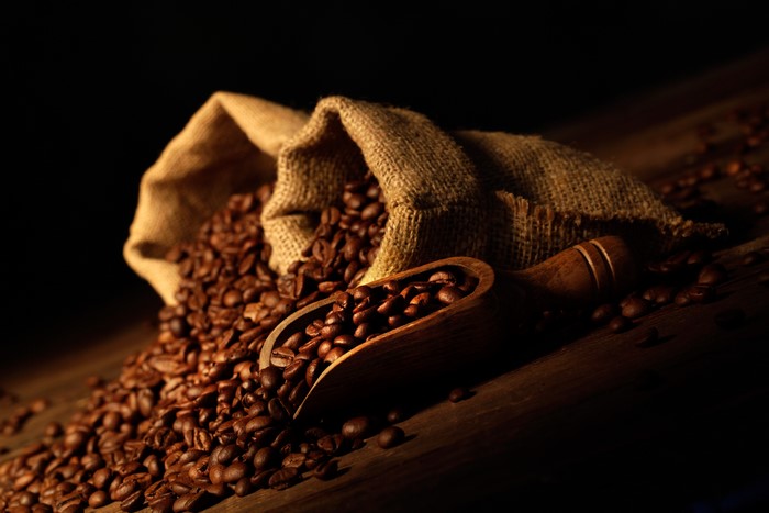 Coffee beans spilling from a burlap sack with a wooden scoop