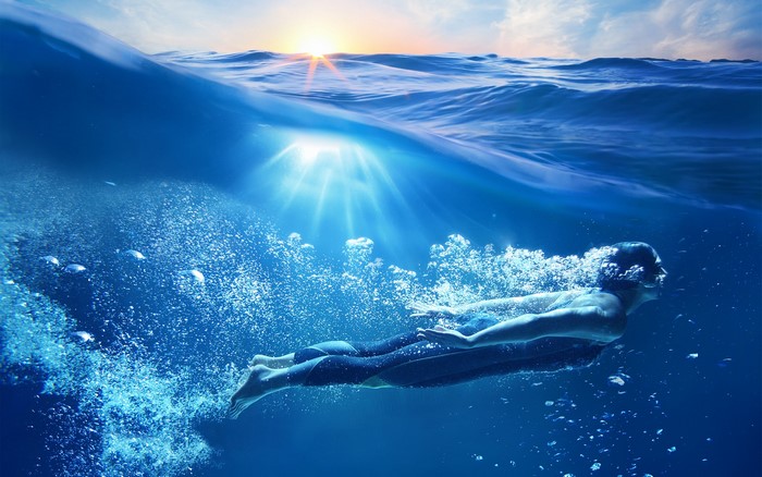 Man swimming underwater with sun rays
