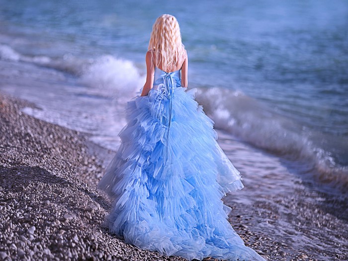 Blonde girl in a blue dress on a pebble beach