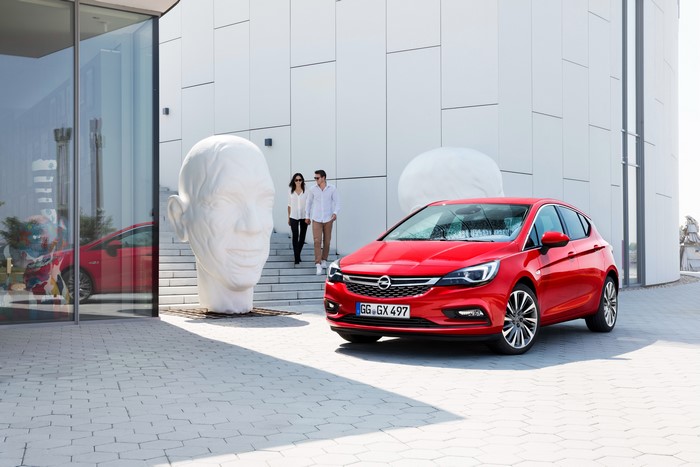 Red Opel Astra K with couple and sculptures