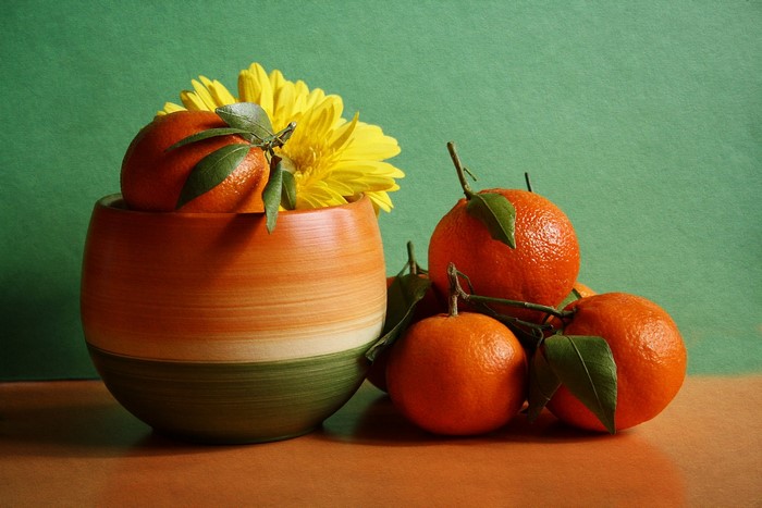 Oranges and yellow flower in a vase