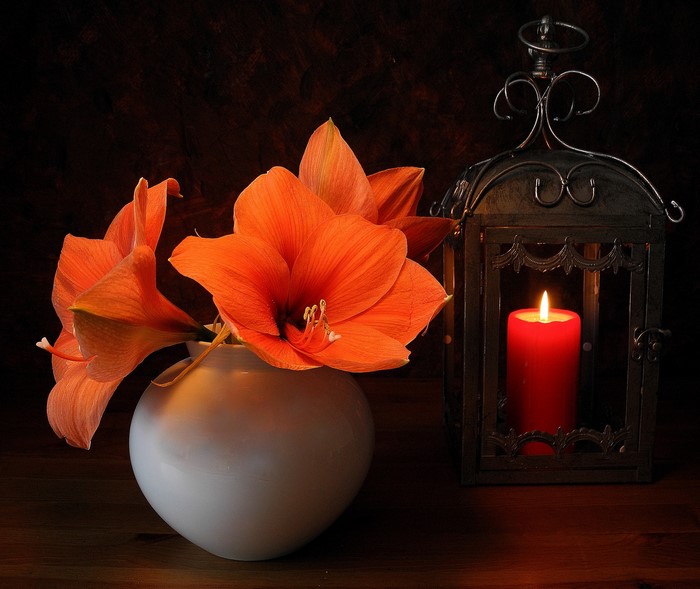 Orange lilies in a white vase next to a lit candle in a lantern