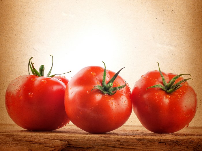 Three ripe tomatoes with water droplets on a wooden surface