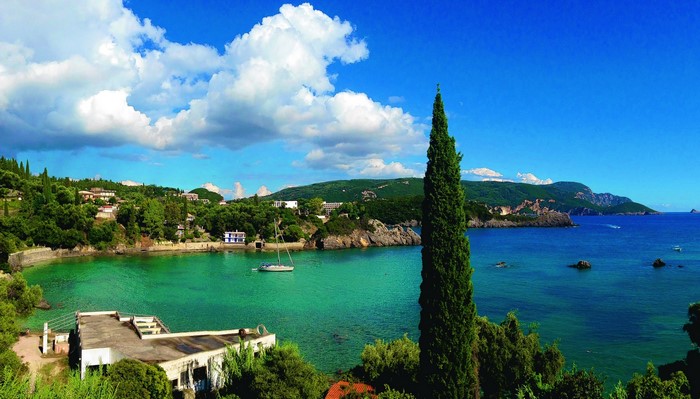 Coastal bay with a sailboat and cypress tree in Corfu, Greece