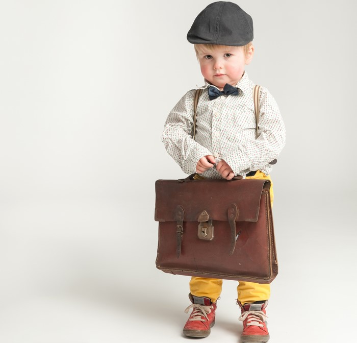Boy in formal shirt and cap holding a handbag