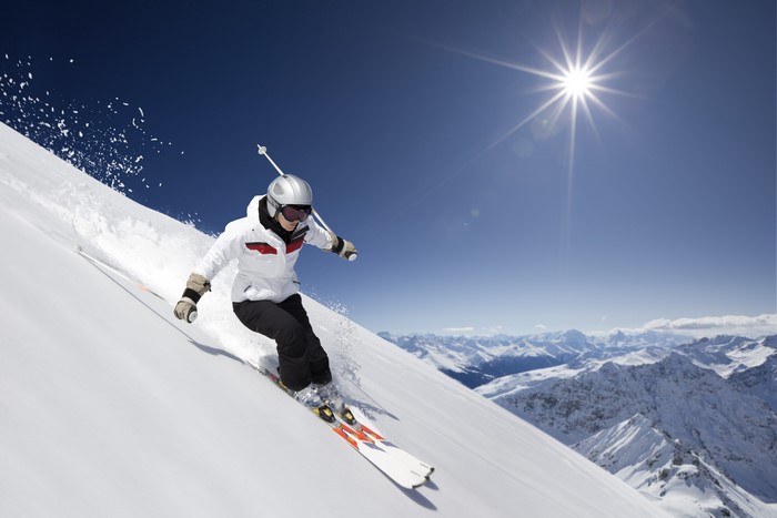 Woman skiing down a snowy mountain under a bright sun