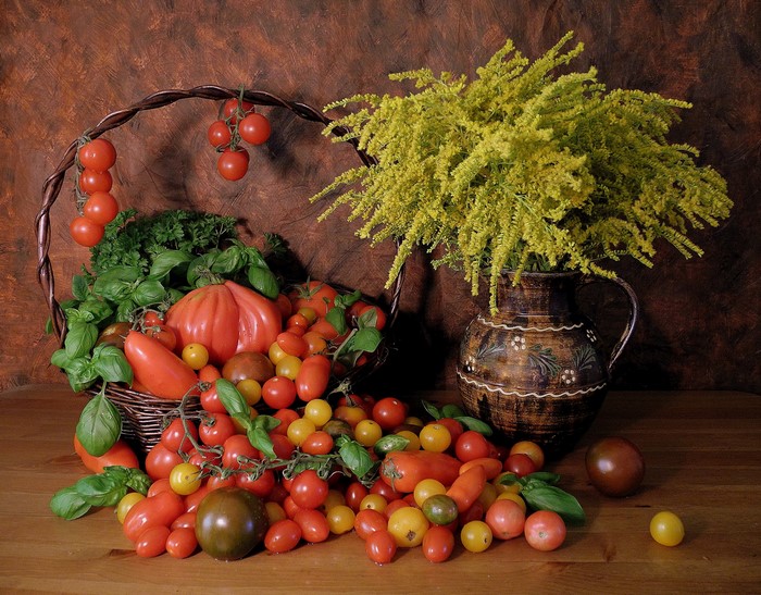 Still-life of tomatoes in a wicker basket with a jug and flowers