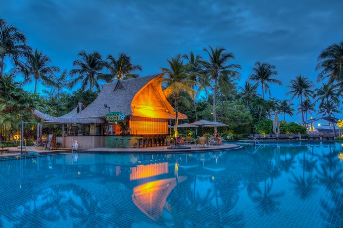 Resort pool and beach bar at dusk with palm trees