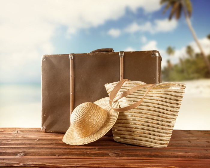 Suitcase, handbag, and hat on a wooden table at the beach