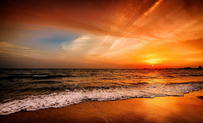 Sunset over the ocean with waves crashing on the beach
