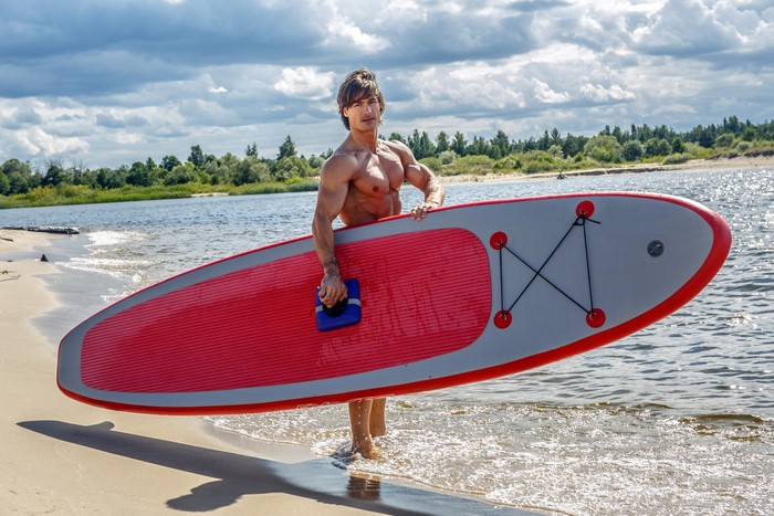 Man holding a paddleboard on a beach