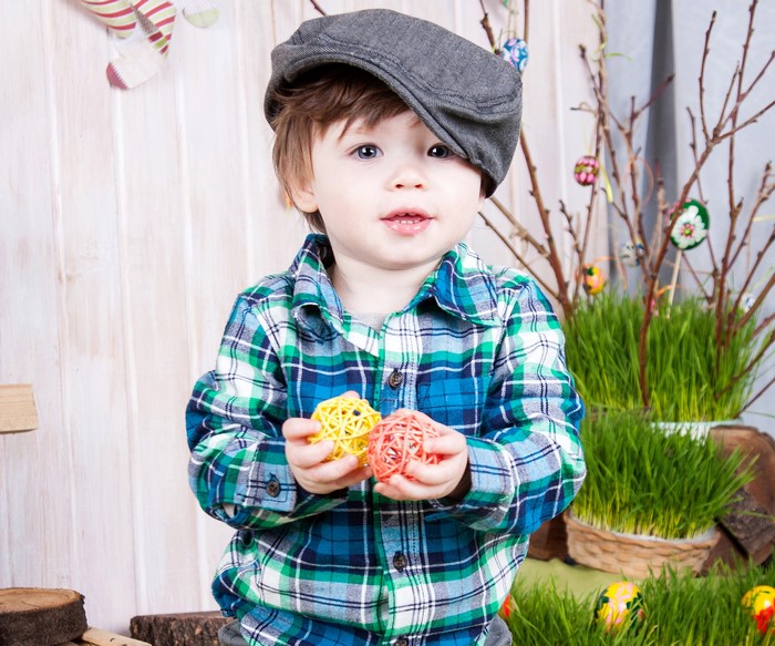 Toddler boy in a plaid shirt and cap holding Easter decorations