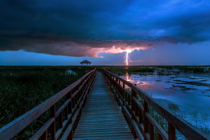 Wooden boardwalk through a marsh during a lightning storm