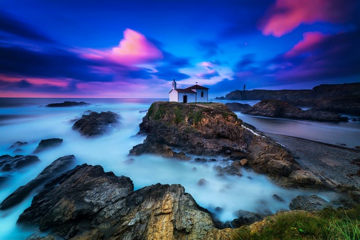 Chapel on a rocky coast at dusk with lighthouse
