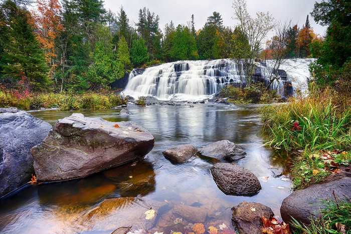 Waterfall cascading over rocks with autumn trees and river