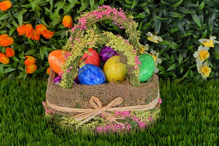 Easter basket with colorful eggs and flowers on grass