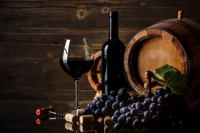 Wine bottle, glass, barrel, and grapes on a reflective surface