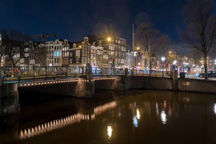 Amsterdam canal bridge at night with houses and reflections