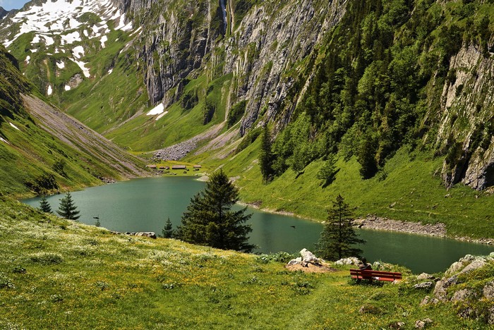 Lake in a mountain valley with green slopes and snow patches