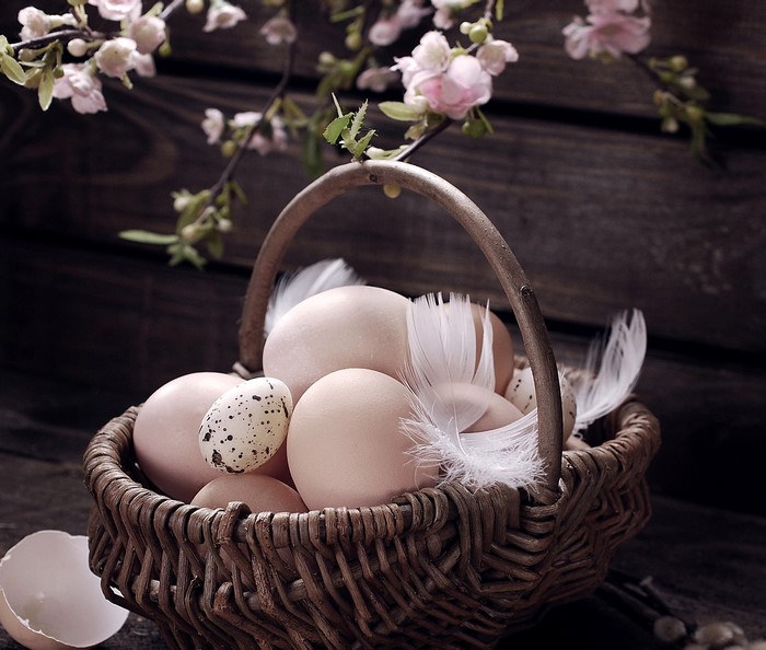 Easter eggs in a wicker basket with feathers and flowers