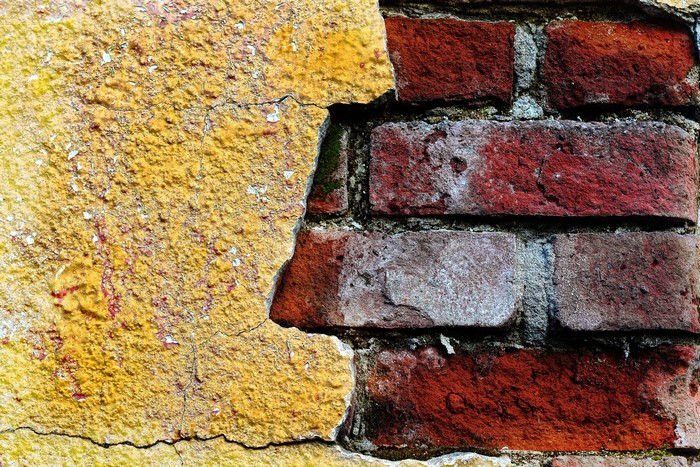 Cracked yellow plaster on a red brick wall texture