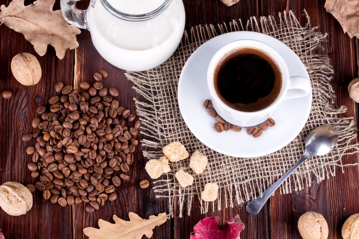 Coffee beans, cup of coffee, milk, walnuts, and autumn leaves