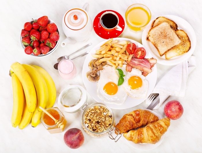 Breakfast with eggs, bacon, fries, toast, croissants, fruit, and coffee