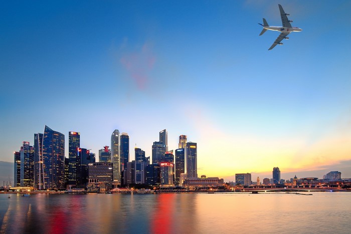 Airplane flying over Singapore skyline at sunset