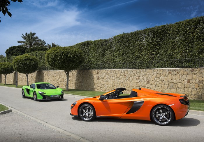 Two McLaren sports cars, one orange convertible and one green coupe