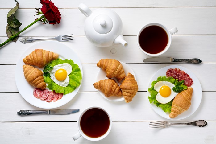 Breakfast with croissants, fried eggs, sausage, and tea