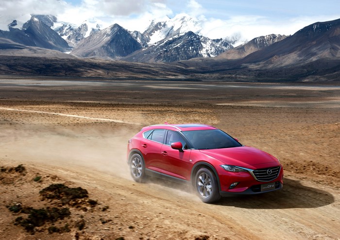Red Mazda CX-4 driving on a dirt road with mountains