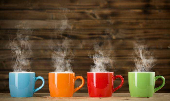 Four steaming mugs of coffee on a wooden table