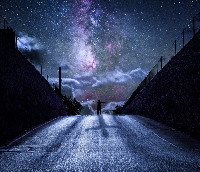 Silhouette of a person on a road under the Milky Way