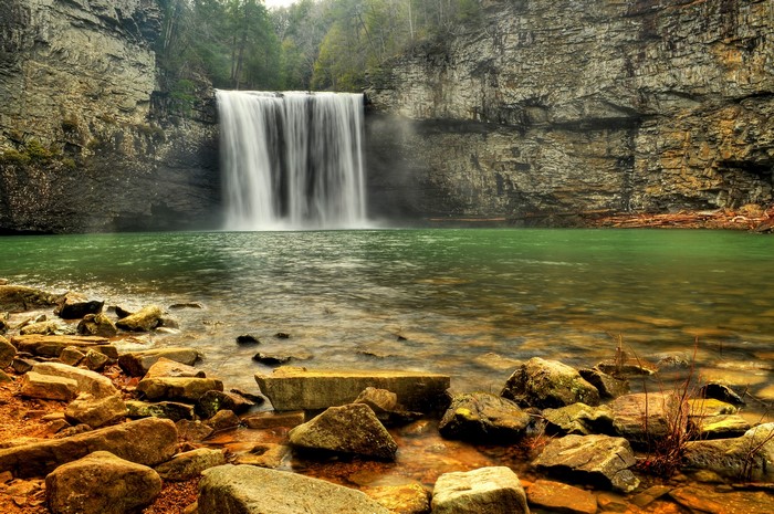 Waterfall cascading into a green pool with rocky shore
