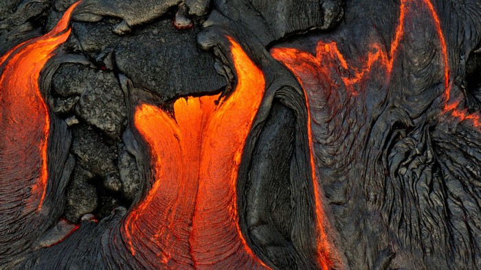Molten lava flowing over dark volcanic rock