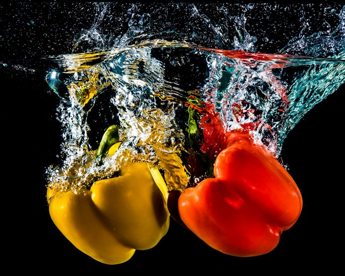 Red and yellow bell peppers splashing into water
