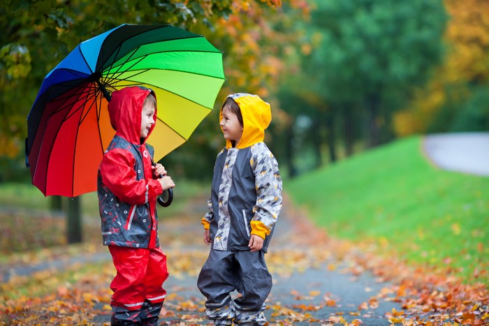 Two boys with a rainbow umbrella in autumn