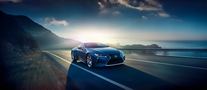 Blue Lexus LC driving on a coastal road at sunset