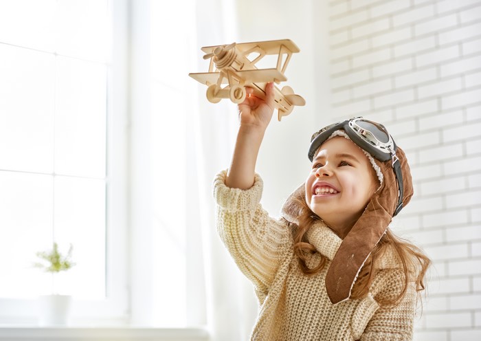 Little girl in pilot hat holding toy airplane