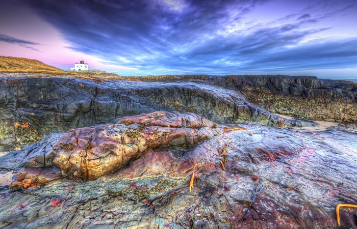 Bamburgh Beach Lighthouse on rocky coast under dramatic sky