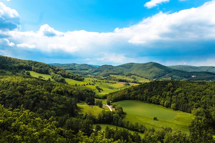Green rolling hills and forests under a blue sky with clouds
