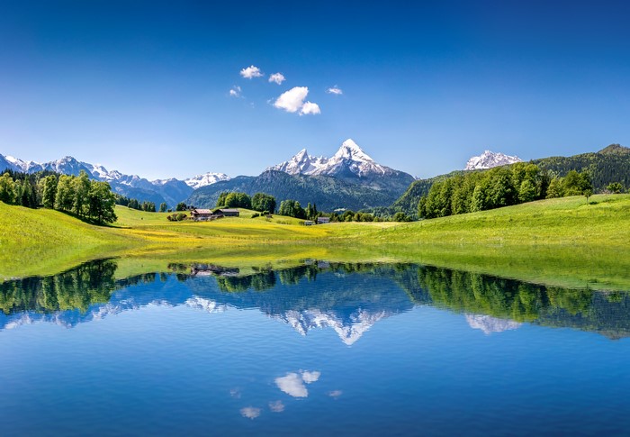 Lake reflection of snow-capped mountains and green grasslands